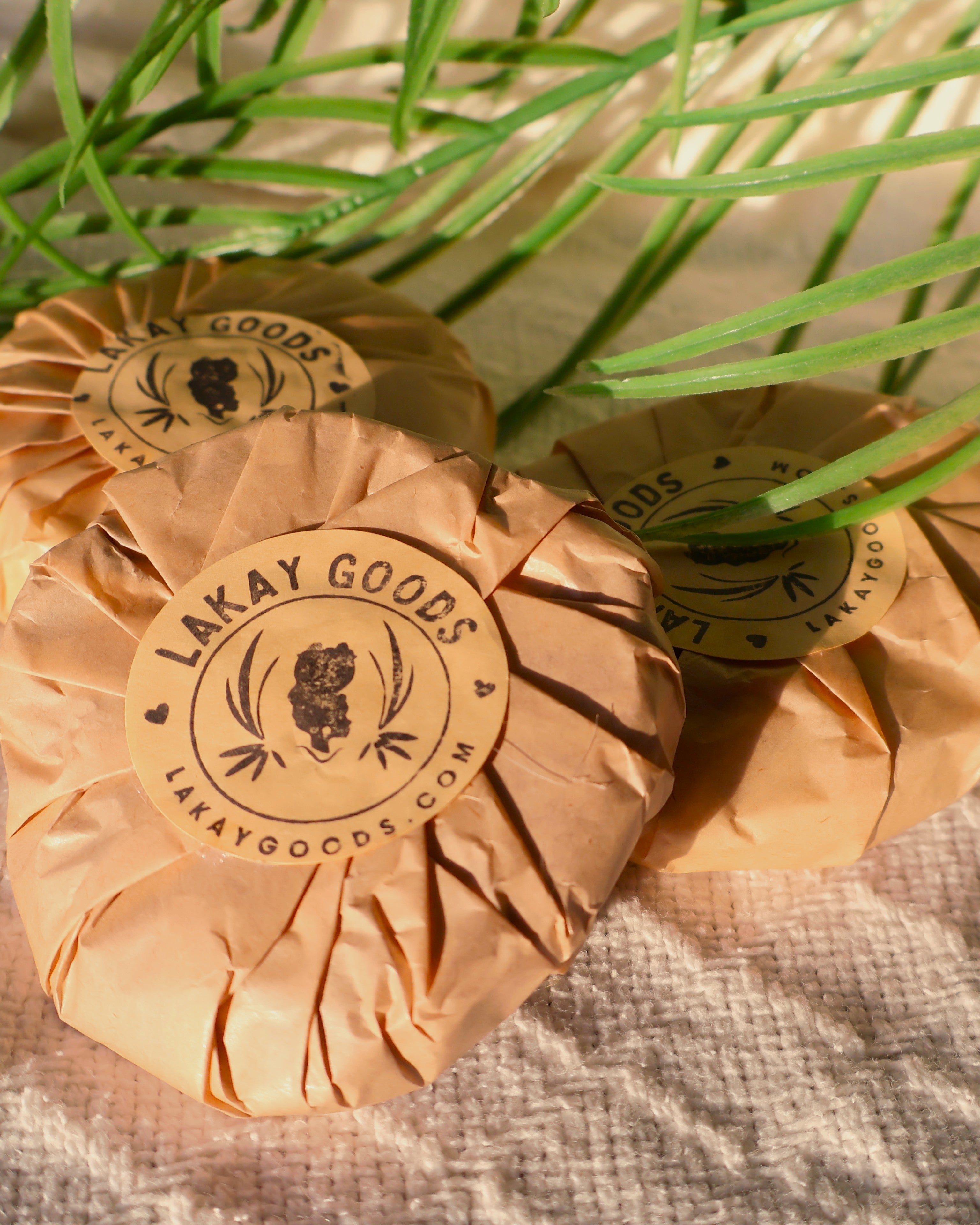 Two wrapped products with 'Lakay Goods' branding on a textured surface with green leaves.