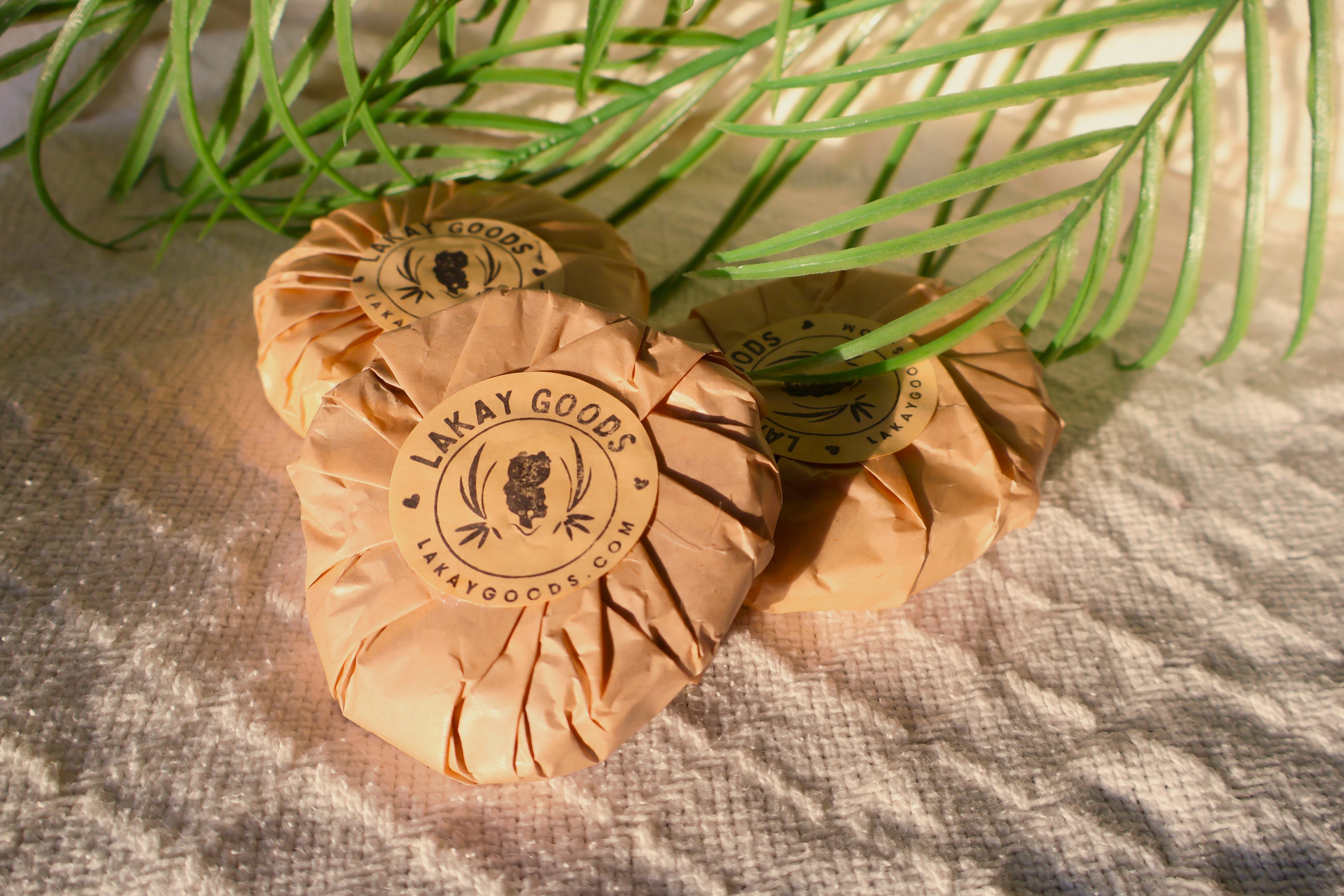 Two wrapped products with 'Lakay Goods' branding on a textured surface with green leaves.